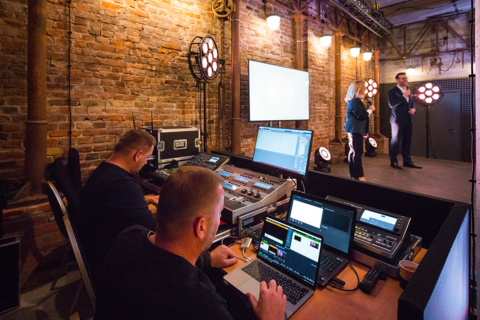 SmartCrew Veranstaltungstechniker bei der Arbeit an Technik während im Hintergrund jemand auf der Bühne bei einem Corporate Event steht